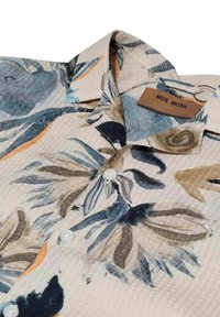 Marškinių tipo palaidinė su apykakle, mėlyno, smėlio spalvos ir oranžinio gėlių rašto ant tekstūruotos baltos medžiagos, ant apykaklės vidinės pusės etikete pažymėta MOS MOSH.