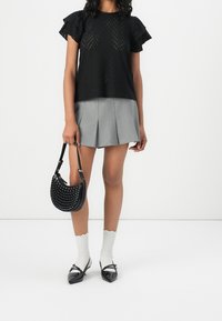 Top perforato nero con maniche volant, gonna grigia plissettata, borsa nera con borchie, calze bianche a coste e scarpe nere in vernice.