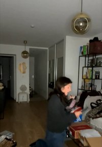 Žena kleči u zatvorenom prostoru držeći više kutija za cipele s policama i visećim svjetlima u pozadini.