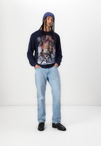 Navy blue sweatshirt with a "Star Wars" graphic, paired with light blue jeans and black shoes, complemented by a knitted blue beanie.