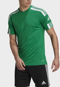 Man som bär en grön Adidas-sporttröja med vita ränder på ärmarna och svarta Adidas-shorts med vita ränder på sidorna.