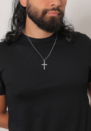 Silver cross pendant on a thin chain, featuring small stones embedded in a vertical and horizontal design, worn with a black t-shirt.