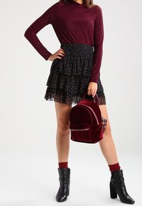 Top de manga larga burdeos, falda de tul negra en capas con puntos plateados y una pequeña mochila de terciopelo rojo. Botas de tacón negras completan el look.