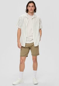 Hemd mit kurzen Ärmeln und blauen vertikalen Streifen auf weißem Hintergrund, kombiniert mit hochgekrempelten khakifarbenen Shorts und weißen Sneakern.