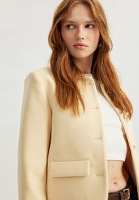 Hellbeige maßgeschneiderte Blazer mit rundem Kragen, Einzelknopfverschluss und einer Brusttasche. Glattes Material mit strukturierter Silhouette.