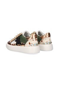 Zapatillas deportivas gruesas de color blanco con acentos en verde, estampado de leopardo, estrella negra, bronce metálico y tachuelas, mostradas desde una vista trasera en ángulo.