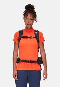 Oranges Sporthemd mit hohem Kragen, kombiniert mit einem schwarzen Rucksack mit mehreren Taschen, der verstellbare Träger und einen Schnallenverschluss hat.