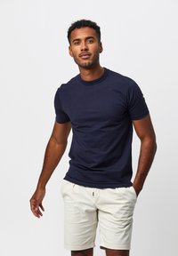 Marineblaue Kurzarm-T-Shirt aus Baumwolle mit Rundhalsausschnitt und normaler Passform, kombiniert mit hellbeigen Shorts.