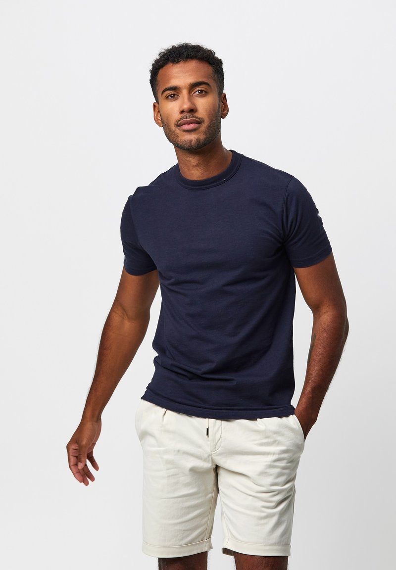 Marineblaue Kurzarm-T-Shirt aus Baumwolle mit Rundhalsausschnitt und normaler Passform, kombiniert mit hellbeigen Shorts.