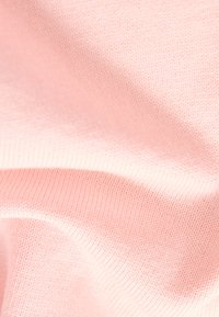 Tissu rose clair texturé avec une finition douce et tricotée. Le matériau a une légère élasticité et présente des motifs de couture fins et visibles.