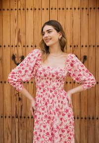 Bloemige midi-jurk met pofmouwen, met een roze patroon op een lichte achtergrond, ruche-borstvoeding en knoopdetails.