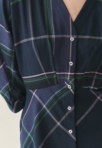 Tengerészes kockás ingruha zöld, rózsaszín és fehér kockákkal, V nyakkivágással, rövid ujjakkal és gombos záródással elöl.