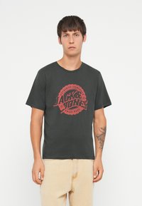 Mørkegrå t-skjorte med korte ermer som har et stort rødt grafisk trykk med teksten "JACK & JONES", rund halsutskjæring og avslappet passform.