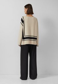 Beżowy, oversize sweter z czarnymi paskami, dzianinowa tekstura, okrągły dekolt, w połączeniu z szerokimi czarnymi spodniami.
