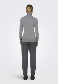 Pull à col roulé gris avec une coupe ajustée, associé à un pantalon ample à carreaux. Des chaussures noires à semelle épaisse complètent le look.