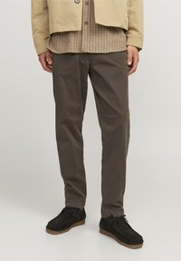 Beżowa kurtka nałożona na brązową, kratkowaną koszulę, zestawiona z ciemnobrązowymi spodniami i czarnymi zamszowymi butami na gumowej podeszwie.