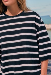 Black and white striped t-shirt with a loose fit, short sleeves, and a rounded neckline, displayed against a coastal background.