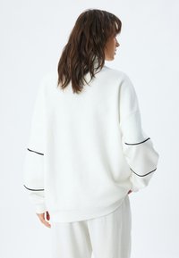 Sudadera blanca de gran tamaño con un cuello alto, hombros caídos, rayas de acento negras en las mangas y puños y dobladillo acanalados.