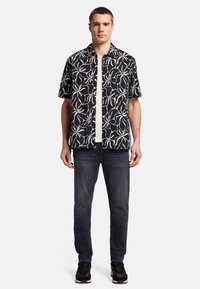 Kortärmad svart skjorta med vitt blommönster, bärs över en ljusgrå t-shirt, ihop med mörka jeans och svarta sneakers.