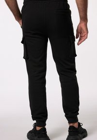 Schwarze Cargo-Hosen mit elastischen Bündchen, ausgestattet mit seitlichen Taschen und einer glatten Textur. Getragen mit schwarzen Sportschuhen.