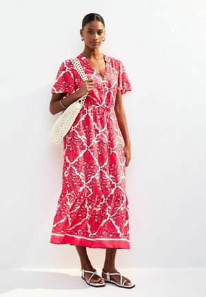 Maxi dress in red with white floral pattern, short ruffled sleeves, cinched waist, and tiered hem. Paired with a woven bag and sandals.