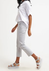 Biała koszula z guzikami, wzorzyste spodnie  typu cropped w szaro-białe wzory oraz szare platformy na sandały z regulowanymi paskami.