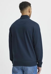 Sötétkék pulóver magas gallérral és hosszú ujjal, sima textúrával, bordázott mandzsettákkal és aljjal. Egyszerű és minimalista dizájn.