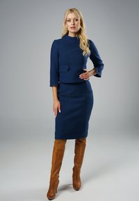 Granatowa, dopasowana sukienka z 3/4 rękawami i bocznymi guzikami, zestawiona z brązowymi skórzanymi botkami sięgającymi do kolan. Gładka tekstura na całej powierzchni.