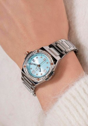 Stainless steel watch with a light blue dial, crystal accents, and Roman numerals. Features a silver band and a rose gold crown.