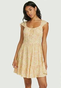 Vestido floral com decote quadrado, mangas curtas com pregas e cintura elástica. Apresenta uma base amarelo claro com padrões em rosa e verde.