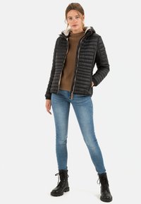 Sort quiltet jakke med hætte og kremfarvet for, parret med en brun sweater og blå jeans, med sorte snørebåndsstøvler.
