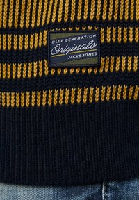 Mörkblå stickad tröja med gula horisontella ränder; har en märkespatch med texten "Blue Generation Originals Jack & Jones."