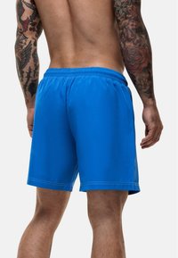 Pantaloni da mare blu con vita elastica, texture liscia e tasche laterali. Presentano un design semplice con dettagli di cucitura a contrasto.