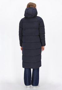 Cămașă puffer de marină cu glugă, cu un design quilted orizontal, mâneci lungi și o siluetă până la genunchi, realizată dintr-un material moale.