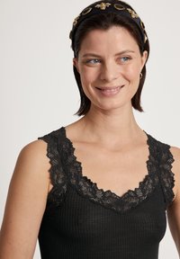 Canotta nera a coste con intricate rifiniture in pizzo lungo il collo e le spalle. Tessuto liscio, design aderente con un look casual.