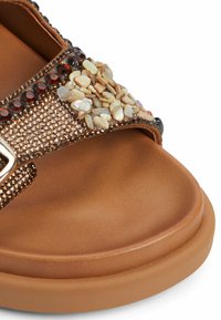 Sandale marron avec une tige texturée ornée d'embellissements ressemblant à des gemmes, semelle lisse et accent en boucle métallique pour la fermeture.