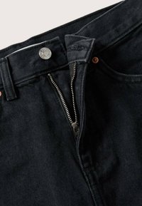 Schwarze Denim-Jeans mit Reißverschluss, silbernen Beschlägen und Kupferrivets. Sie verfügen über einen strukturierten Stoff und ein gesticktes Etikett im Bund.