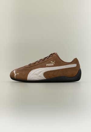 Brauner Wildleder-Puma-Sneaker mit weißem Streifen und Logo, schwarzer Sohle, niedrigem Design und Schnürverschluss, in Seitenansicht gezeigt.