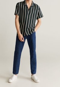 Korte mouwen, donkergroene overhemden met witte verticale strepen, gecombineerd met blauwe spijkerbroek en witte sneakers.