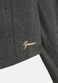 Szary wełniany żakiet w pionowe prążki, z złotym akcentem logo "Guess" na kołnierzu. Miękka tekstura z dopasowanym krojem.
