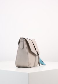 Šedá kožená kabelka s klopovým uzávěrem, černými detaily a modrým peřím jako akcentem. Měkká, hladká textura a strukturovaný tvar.