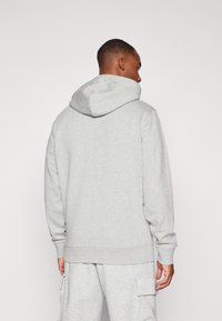 Gray hooded sweatshirt made of soft fabric, featuring a front kangaroo pocket, ribbed cuffs, and waistband. Worn with matching gray pants.