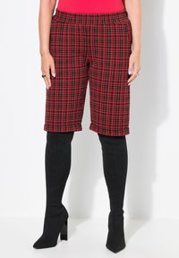 Röd och svart rutiga cropped-byxor med elastisk midja. Bärs med svarta strumpor som går upp till låren och högklackade stövlar. Slät struktur.