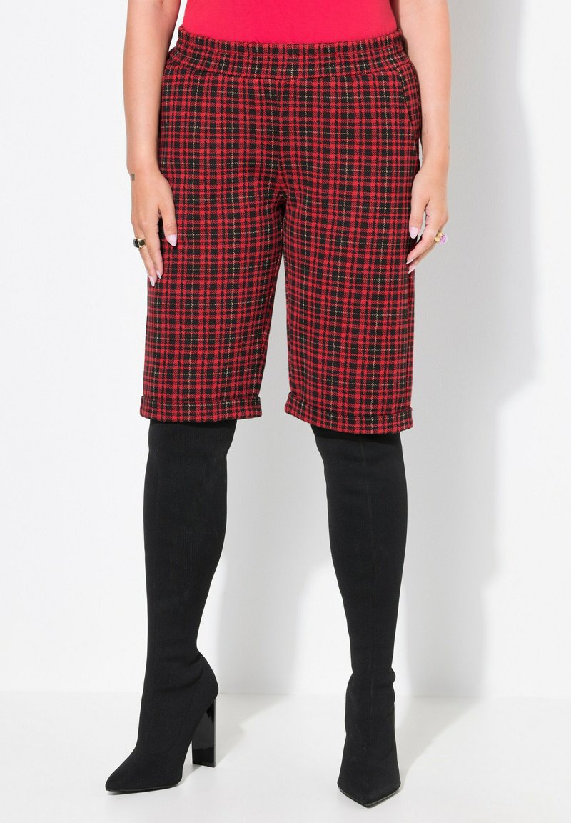 Röd och svart rutiga cropped-byxor med elastisk midja. Bärs med svarta strumpor som går upp till låren och högklackade stövlar. Slät struktur.