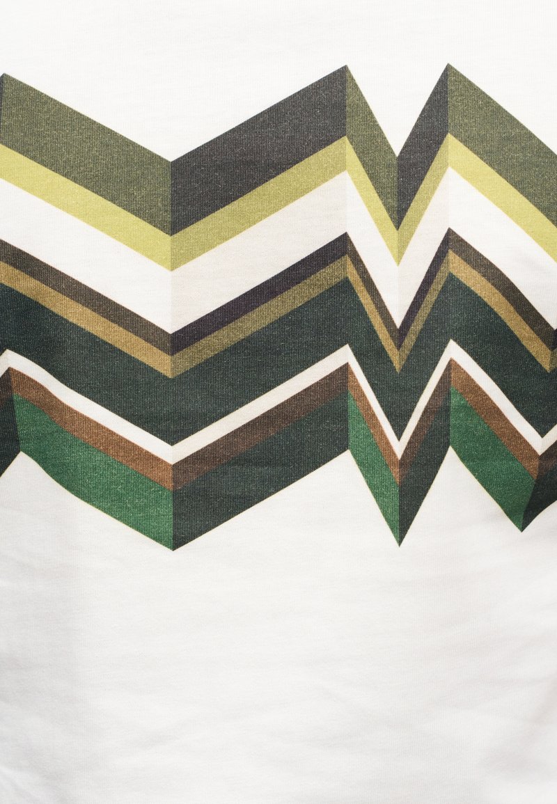 Chevron-patterned fabric with green, brown, and white stripes; made of soft, textured cotton; features sharp angles and layered design.