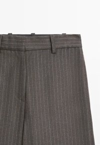 Pantaloni grigi a righe con pinstripe, caratterizzati da una parte frontale piatta, passanti per cintura e una vestibilità sartoriale, realizzati in un tessuto testurizzato con una leggera lucentezza.