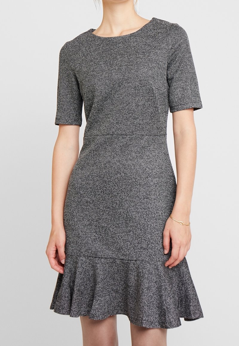 Robe noire et blanche texturée avec un corsage ajusté, des manches courtes et un ourlet évasé. Confectionnée dans un tissu tissé avec un motif subtil.