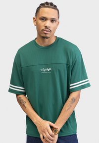 Grønn kortermet mesh t-skjorte med hvite striper på ermene og "Highlight. REDEFINED REBEL" trykt på forsiden. Teksturert stoff.