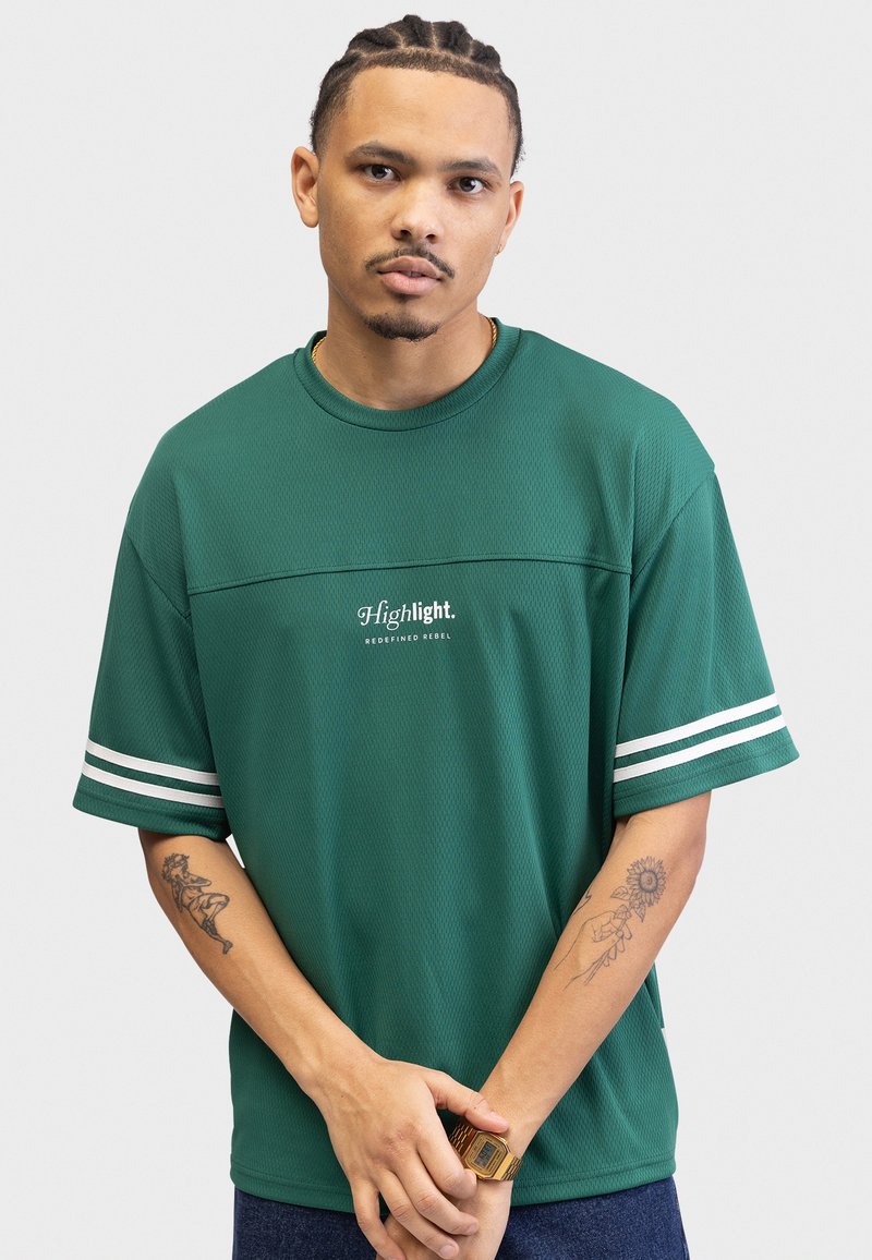 Grønn kortermet mesh t-skjorte med hvite striper på ermene og "Highlight. REDEFINED REBEL" trykt på forsiden. Teksturert stoff.
