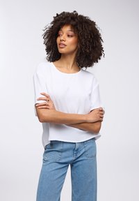 Top bianco a maniche corte con un motivo testurizzato, scollatura rotonda e vestibilità comoda, abbinato a jeans dritti azzurri.